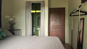 A hotel room with a bed, a mirror, a wooden door, a hanging clothes rack, and a small table with a vase of flowers. - Jungle luxury on a budget,, brand new space (Puerto Carrillo)