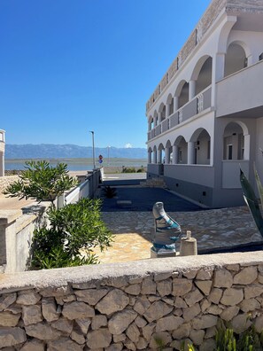 A hotel with a courtyard, stone walls, and a view of the sea and mountains.