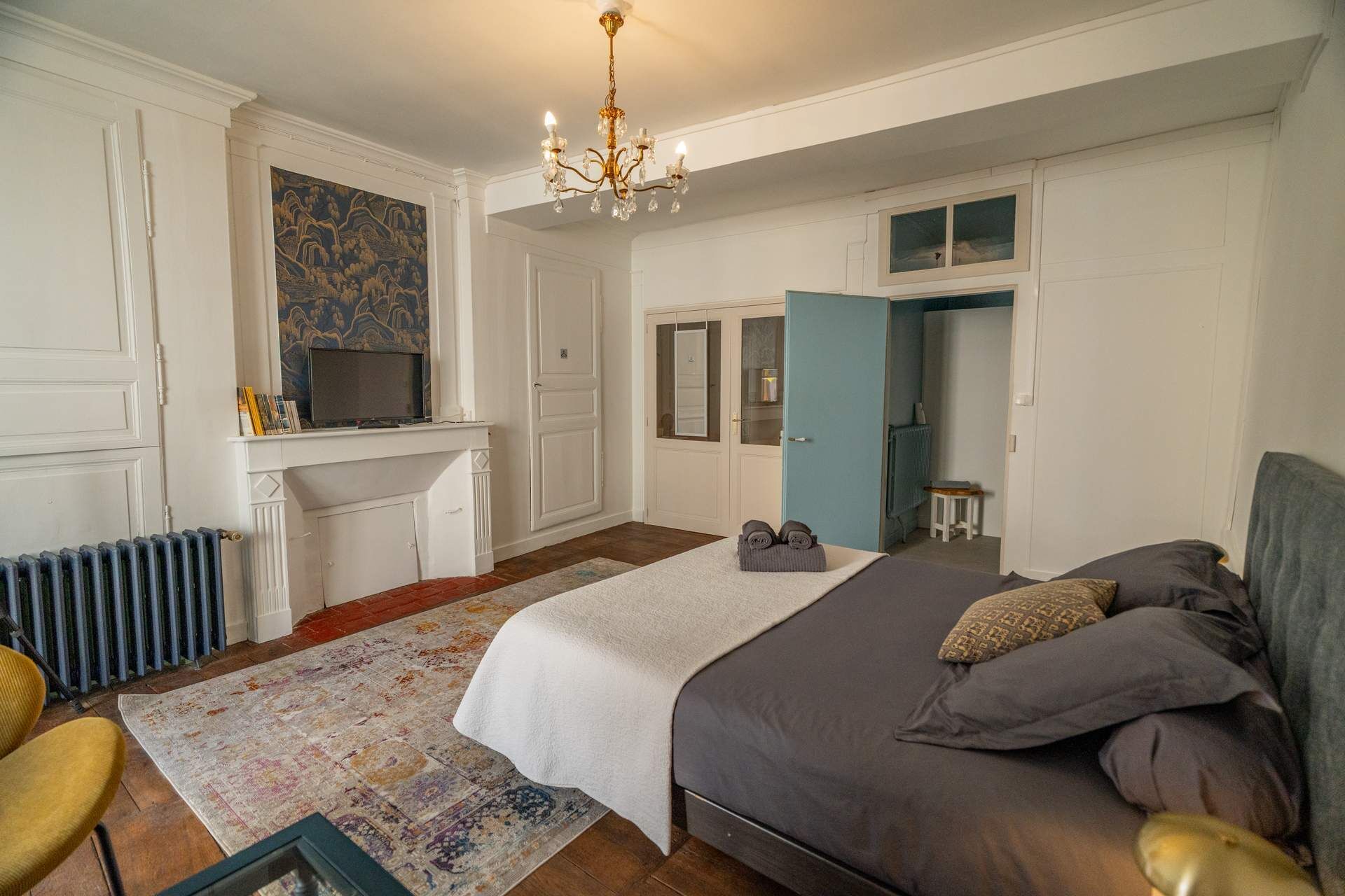 Une chambre à coucher avec un lit, une chaise, un radiateur, un lustre et un tableau au mur.