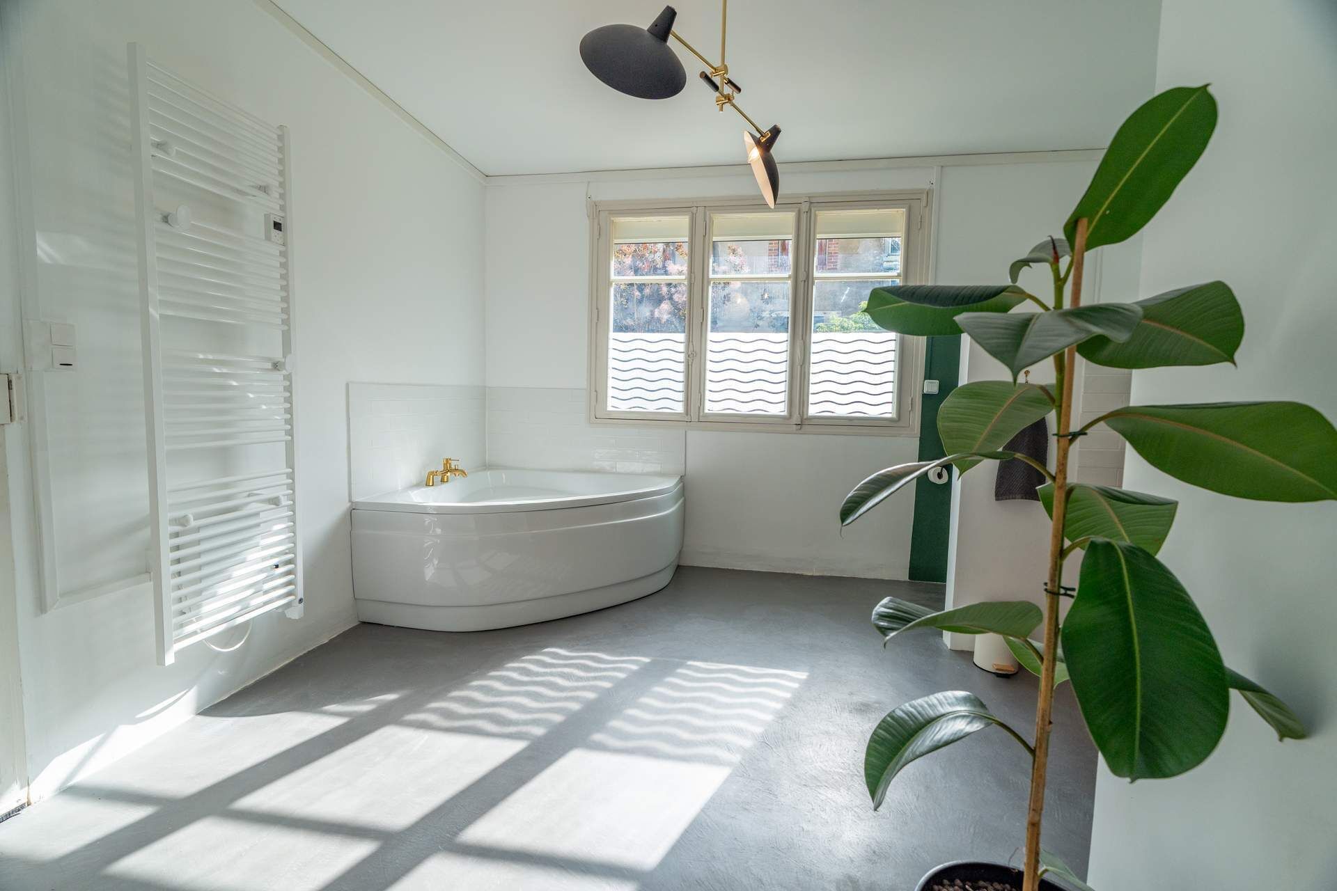 A modern bathroom with a bathtub, a radiator, a window, and a potted plant.