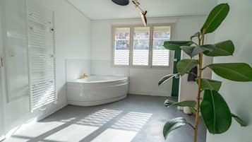 A modern bathroom with a bathtub, a radiator, a window, and a potted plant.