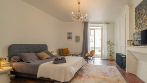 Un dormitorio con cama, mesita de noche, lámpara, silla y vistas al exterior.