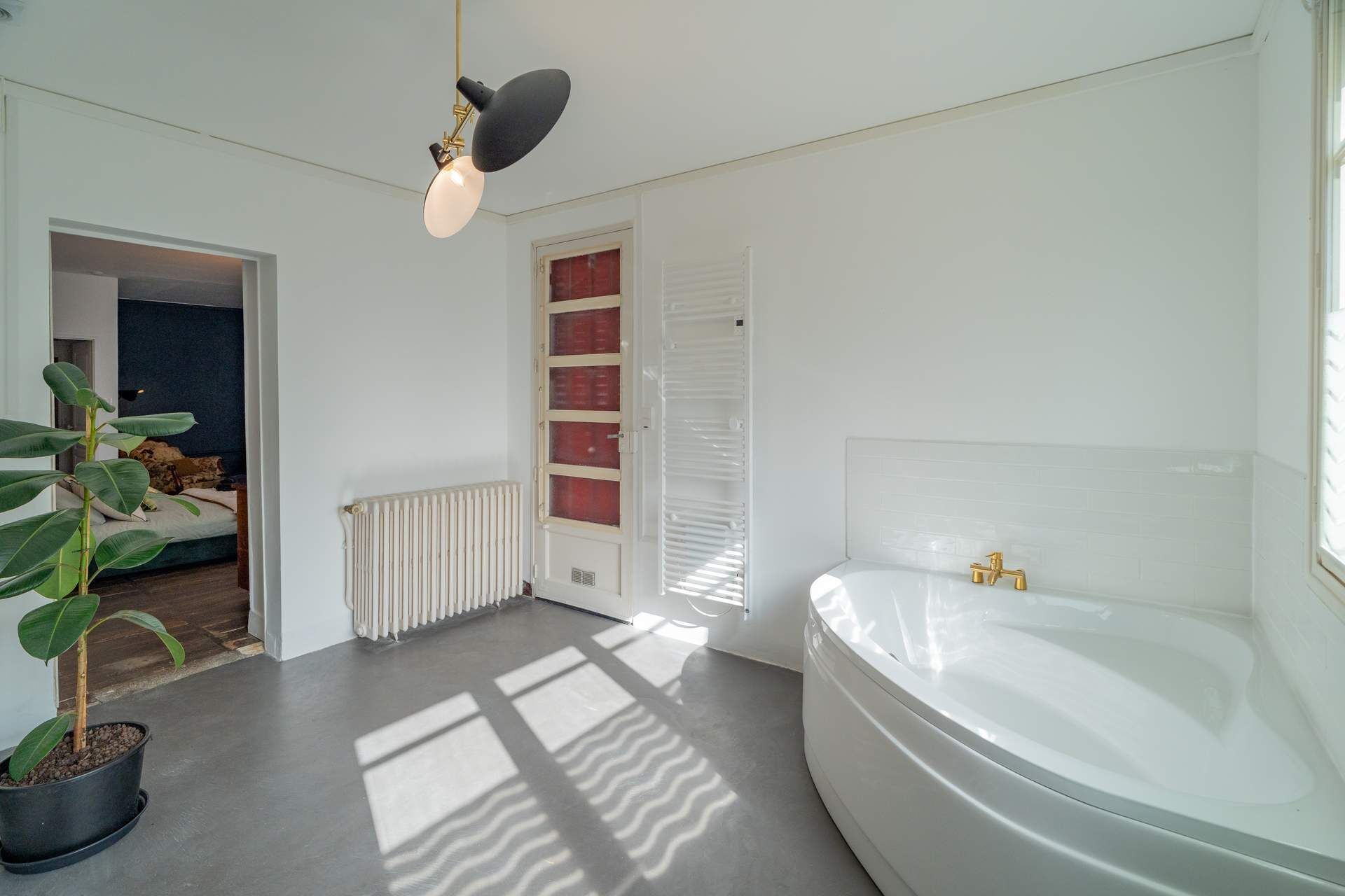 A modern bathroom with a large bathtub, a radiator, and a potted plant.