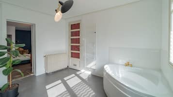 A modern bathroom with a large bathtub, a radiator, and a potted plant.
