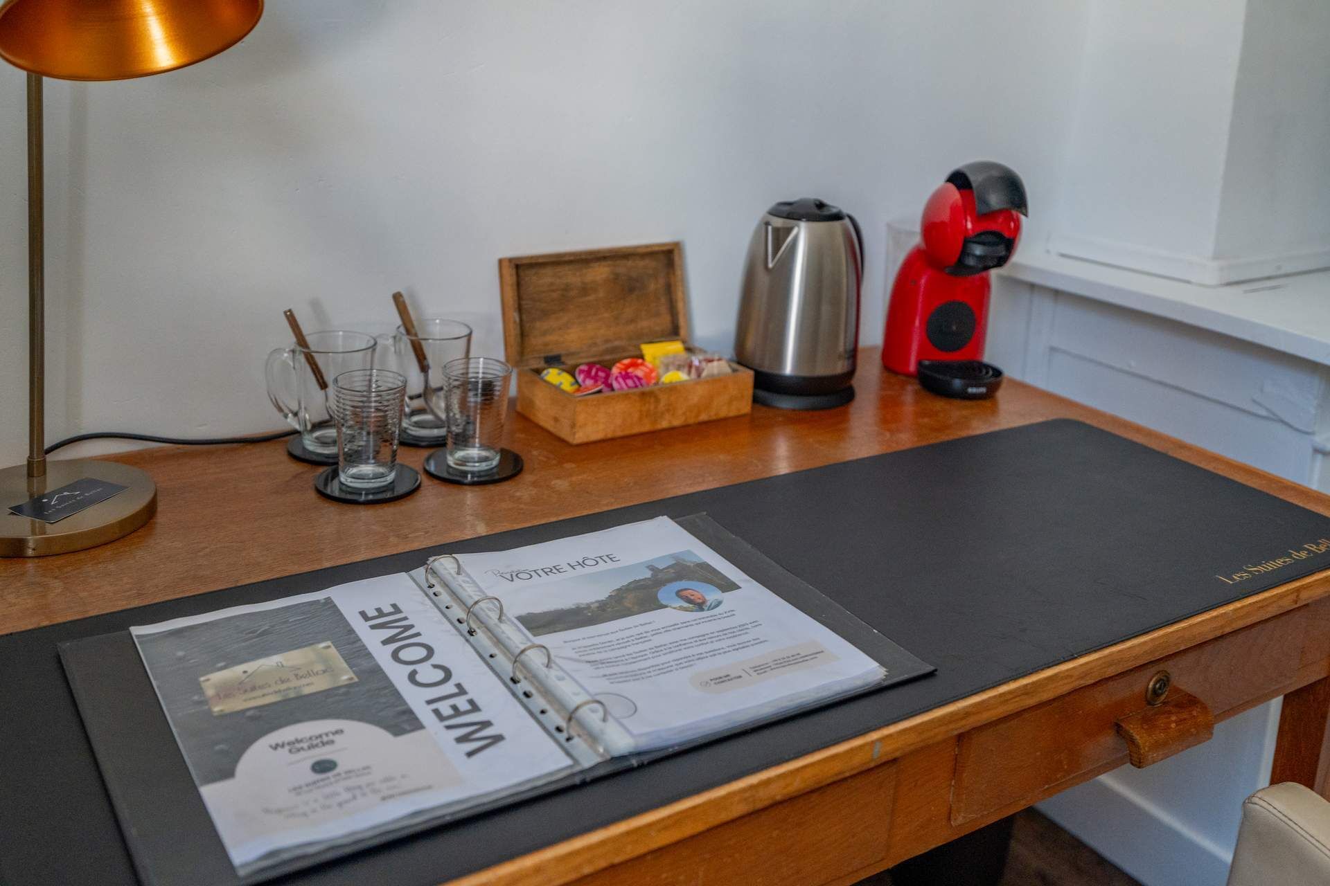 Et skrivebord med en velkomstfolder, kaffemaskine, en rød legetøj og en trækasse med chokolade.