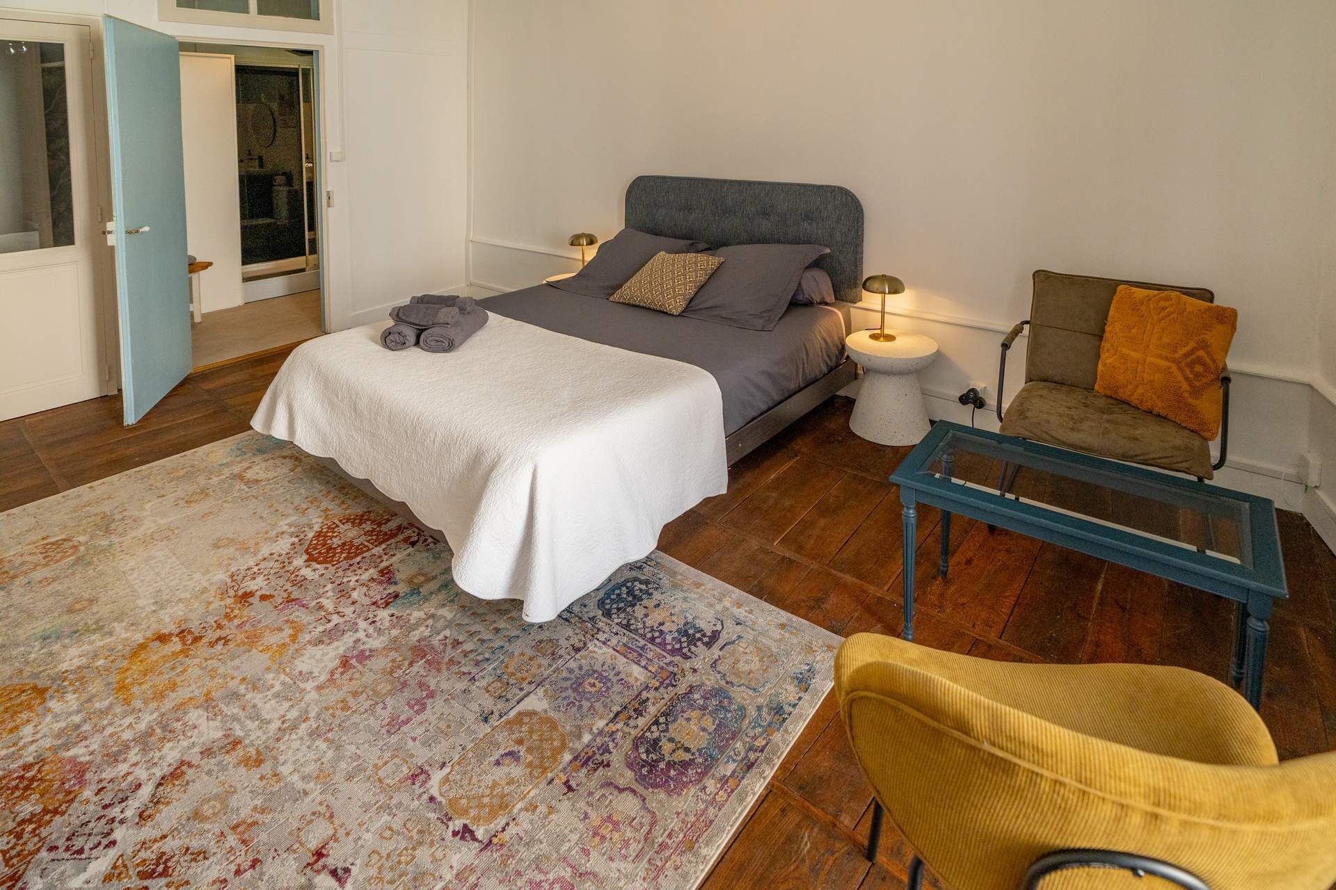 Un dormitorio con cama, mesitas de noche, una silla y una alfombra.