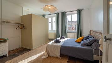 Un dormitorio con cama, una mesita de noche, una lámpara colgante, una ventana con cortinas y vistas a edificios.
