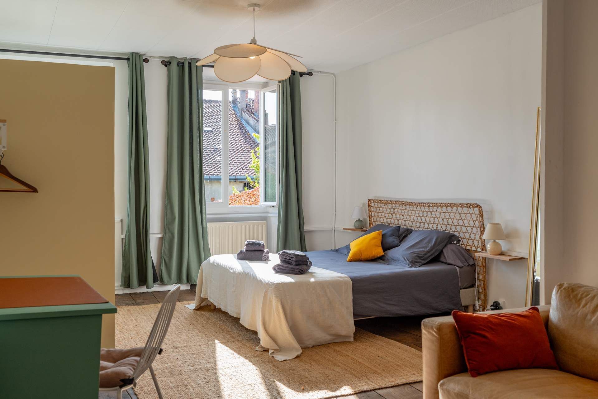 A bedroom with a bed, a chair, a table, and a window with curtains.