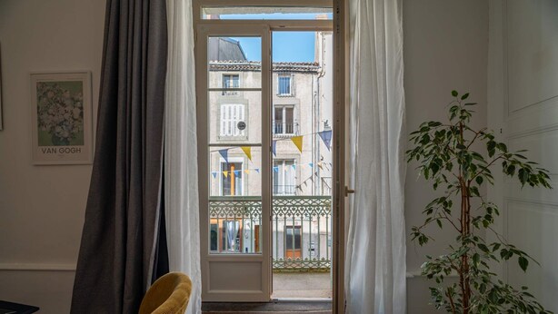 Una habitación con vistas a un balcón a través de una puerta, una planta en maceta y un cuadro en la pared.