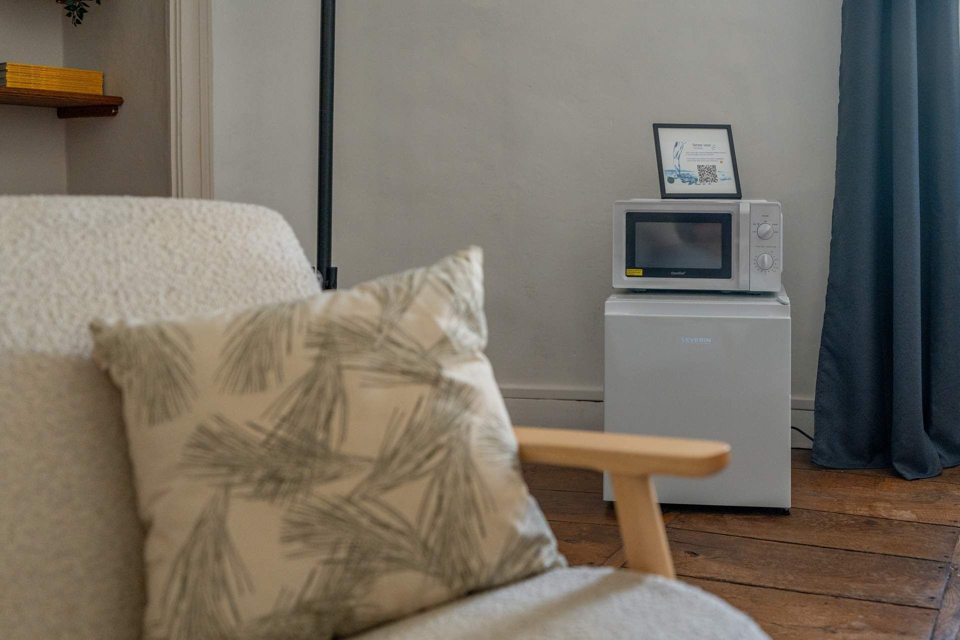 A cozy room with a white sofa, a small white refrigerator, and a microwave on top.