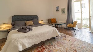 Un dormitorio con cama, dos sillas, una mesa y un balcón.