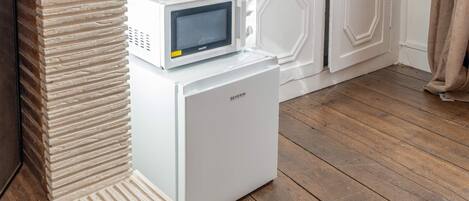 A compact white refrigerator with a built-in microwave on top, placed in a corner against a brick wall.