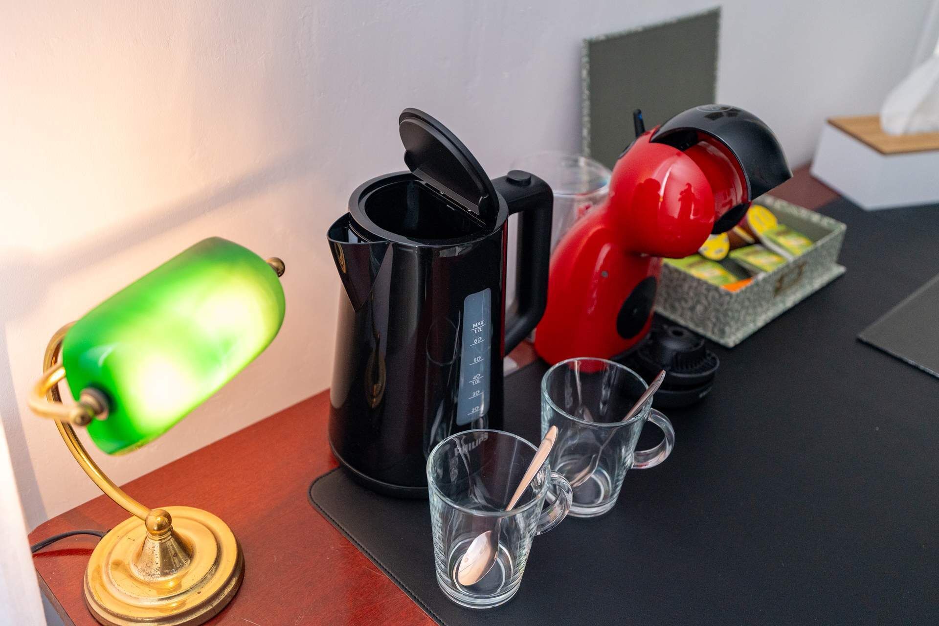Una estación de café con una cafetera, tazas y una lámpara verde.