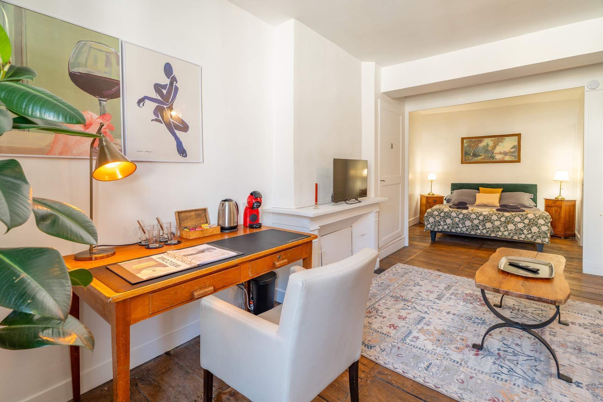 Una habitación de hotel moderna con un escritorio de madera, una silla blanca y una cama con ropa de cama floral.