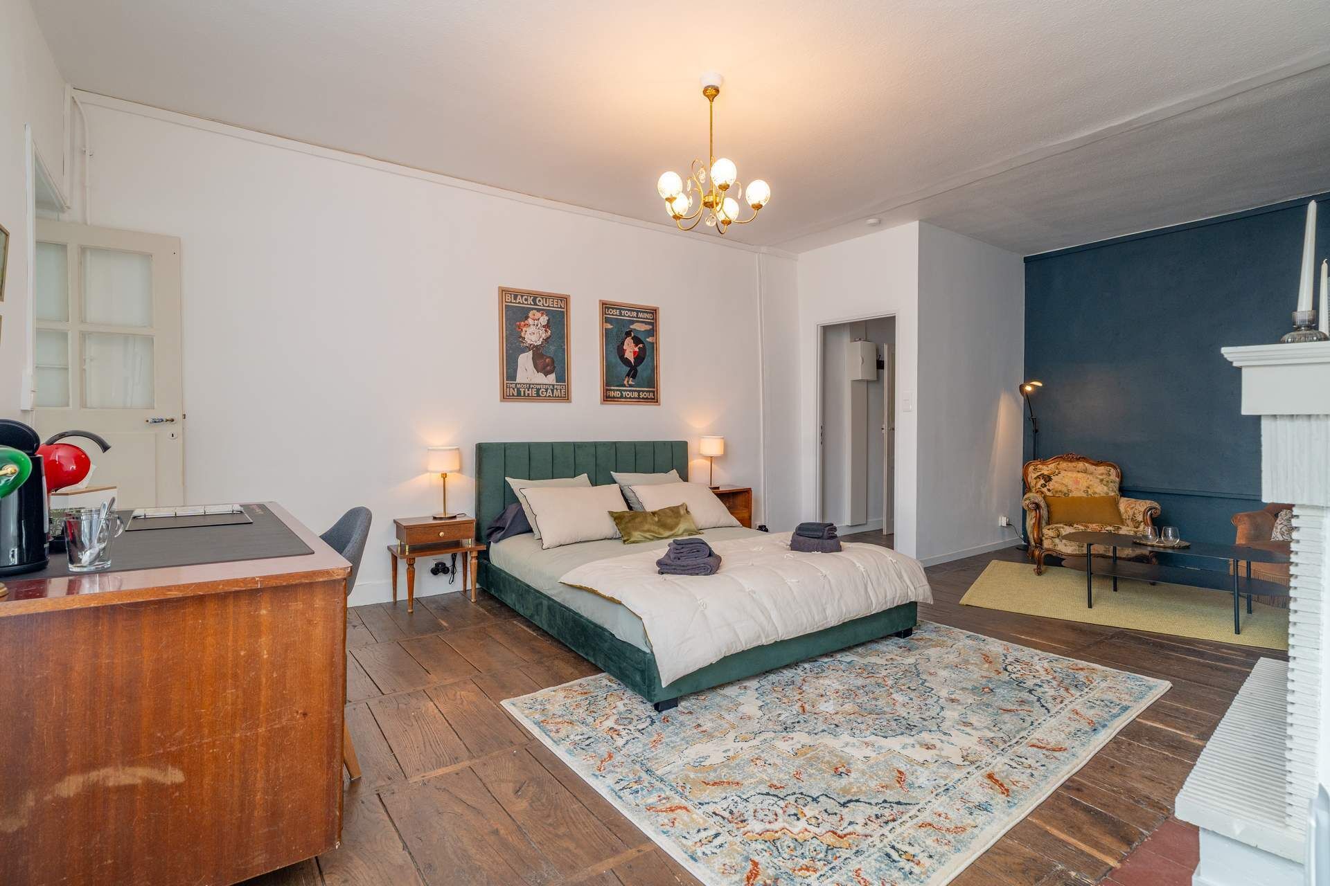 Quarto com cama, mesas de cabeceira, escrivaninha, cadeira, tapete e lustre.