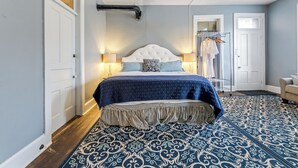 Un dormitorio con una cama grande, dos lámparas de noche, un armario y una alfombra estampada.