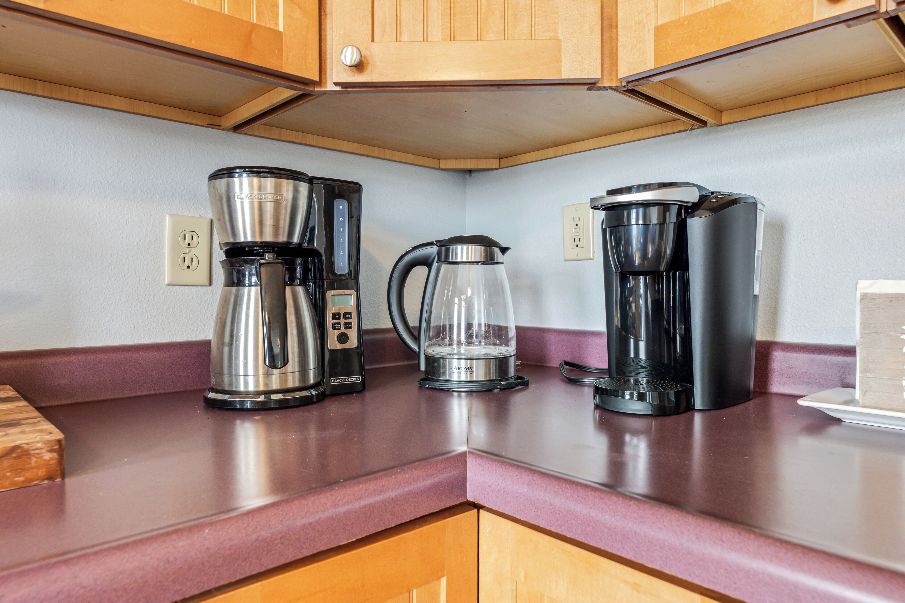 A kitchen with wooden cabinets, a marble countertop, and three coffee makers.