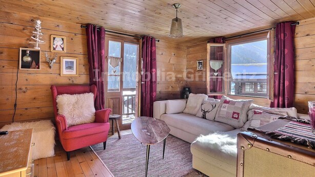 Ein gemütliches Blockhaus-Interieur mit Holzwänden, einem roten Sessel, einem weißen Sofa und einem kleinen Tisch.
