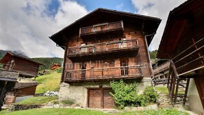 Ein traditionelles Holzhaus mit Steinunterbau, einem Balkon im oberen Stockwerk und einem Steineingang.