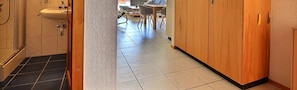 A narrow hallway with a sink, wooden cabinets, and a tiled floor.