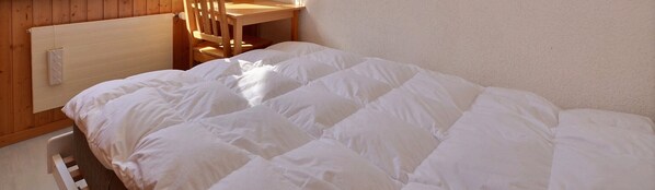 A bed with a white duvet in a room with wooden walls and a wooden chair.