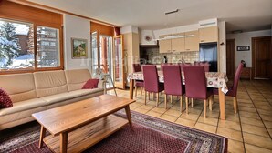 A living room with a sofa, a wooden coffee table, and a dining area with a table and chairs. - Very comfortable flat for 7 people, living room with fireplace, kitchen area with dishwasher, 1 doub (Grimentz)