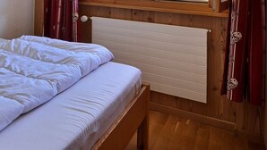 Un letto singolo con biancheria bianca in una stanza con pareti in legno e termosifone.