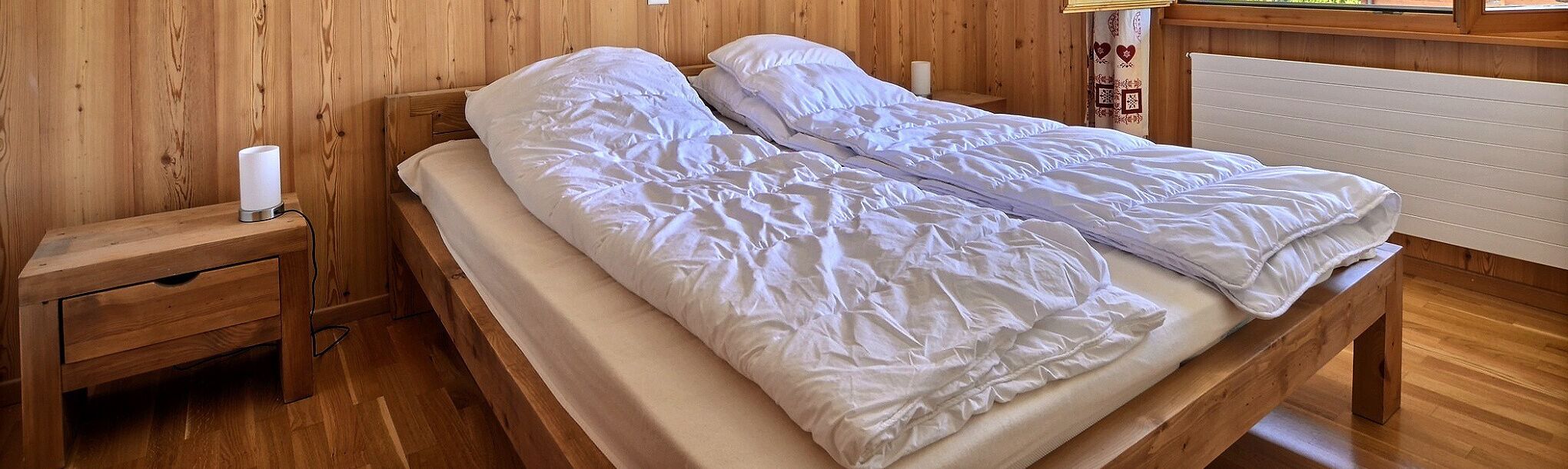 Ein Zimmer mit Holzboden, einem Bett, Nachttischen und einem Fenster mit Vorhängen.