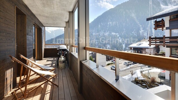 Un balcone in legno con vista su una montagna innevata e un piccolo edificio sullo sfondo.