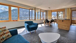 Un soggiorno moderno con una poltrona blu, un tavolino da caffè bianco e vista sulle montagne attraverso ampie finestre.
