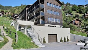 Un hotel moderno a più piani con una scalinata centrale, un garage e vista sulle colline circostanti.