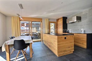 A modern kitchen with wooden cabinetry, a central island, and a dining area with a table and chairs.