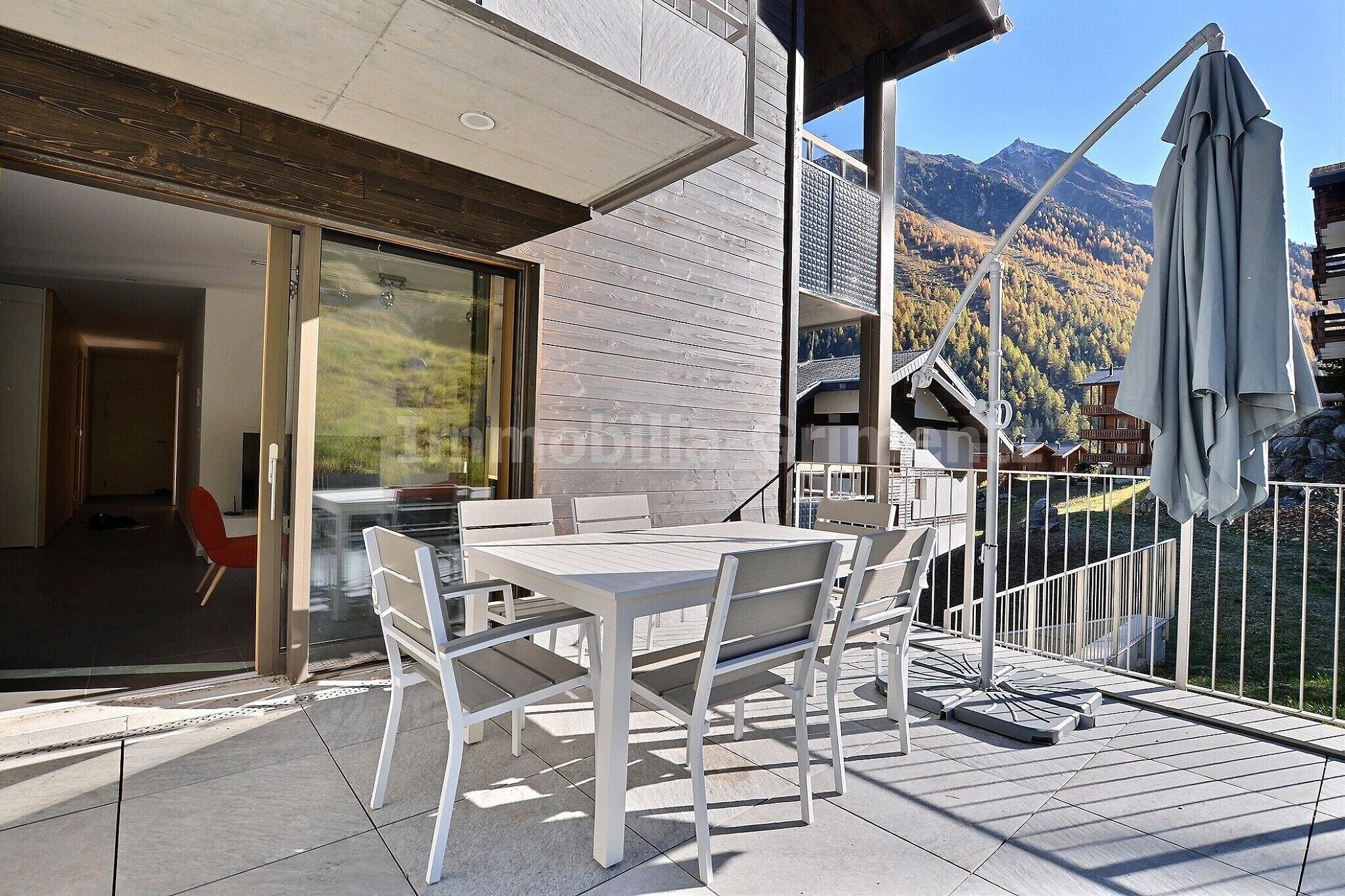 Une terrasse extérieure moderne, dotée d’une table et de chaises, d’une porte-fenêtre coulissante donnant sur un espace intérieur, et offrant une vue sur les montagnes en arrière-plan.