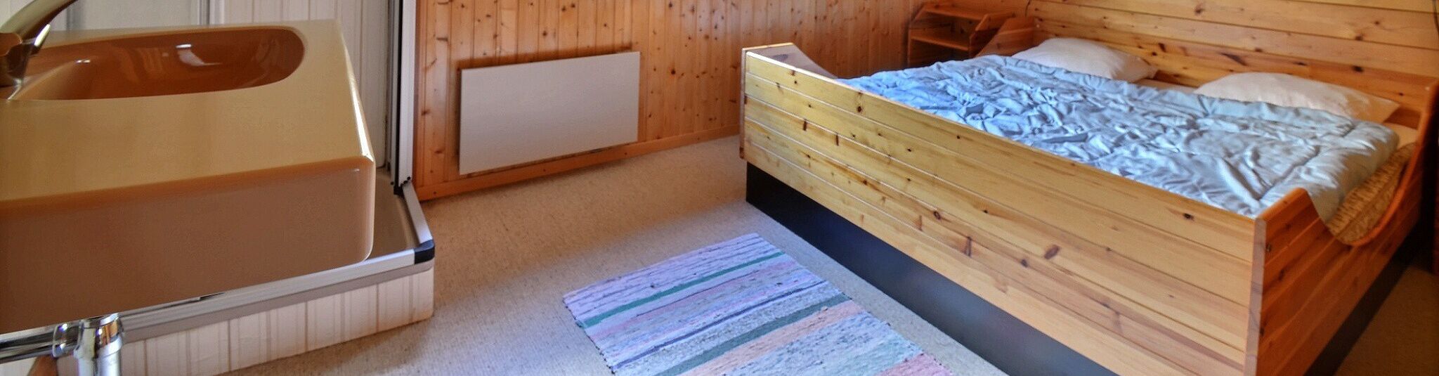 Une chambre à coucher avec un lit en bois, une commode en bois et une salle de bain équipée d’un lavabo et d’un miroir.