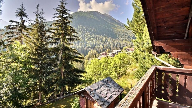 Une cabane en bois dotée d’un balcon donnant sur une vallée boisée et une montagne.
