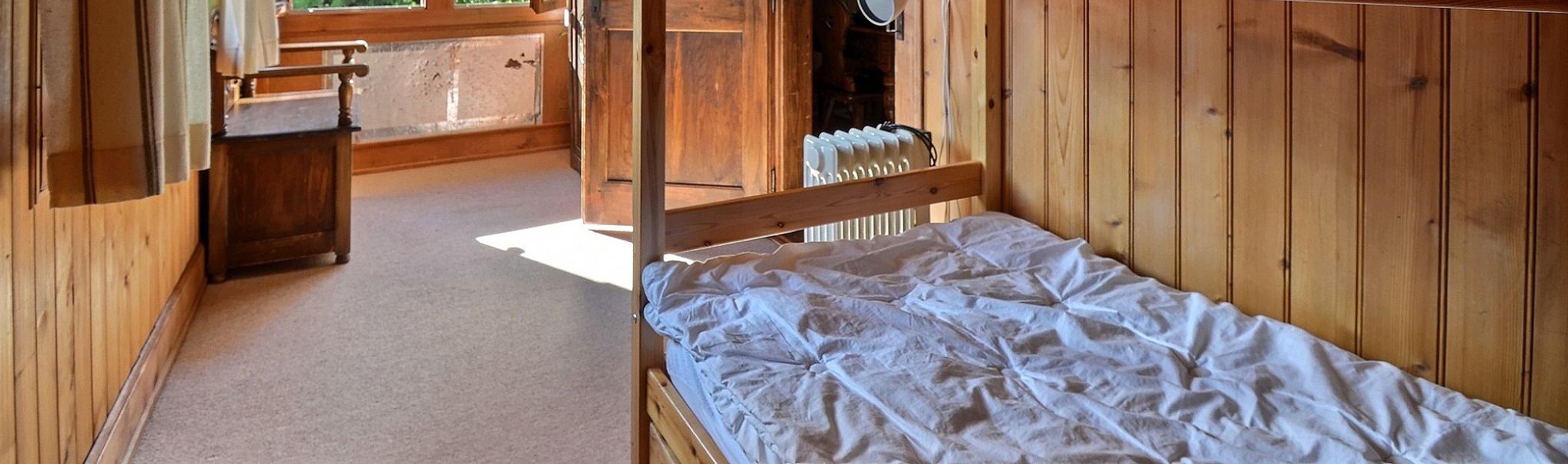 Ein Holzhüttenraum mit einem Einzelbett, einer Holzbank und einer Heizung.