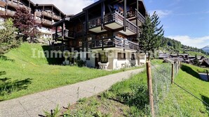 A multi-story building with balconies, a paved path, and a mountainous backdrop.