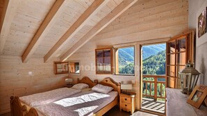 Une chambre à coucher en bois, avec un lit, des tables de chevet et une vue sur un paysage montagneux.