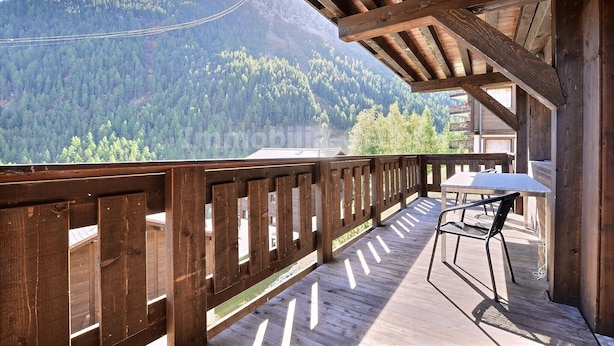 A wooden deck with a table and chair, overlooking a forested mountain range. - Very comfortable flat for 7 people, living room with wood-burner, kitchen area with dishwasher, 2 do (Grimentz)