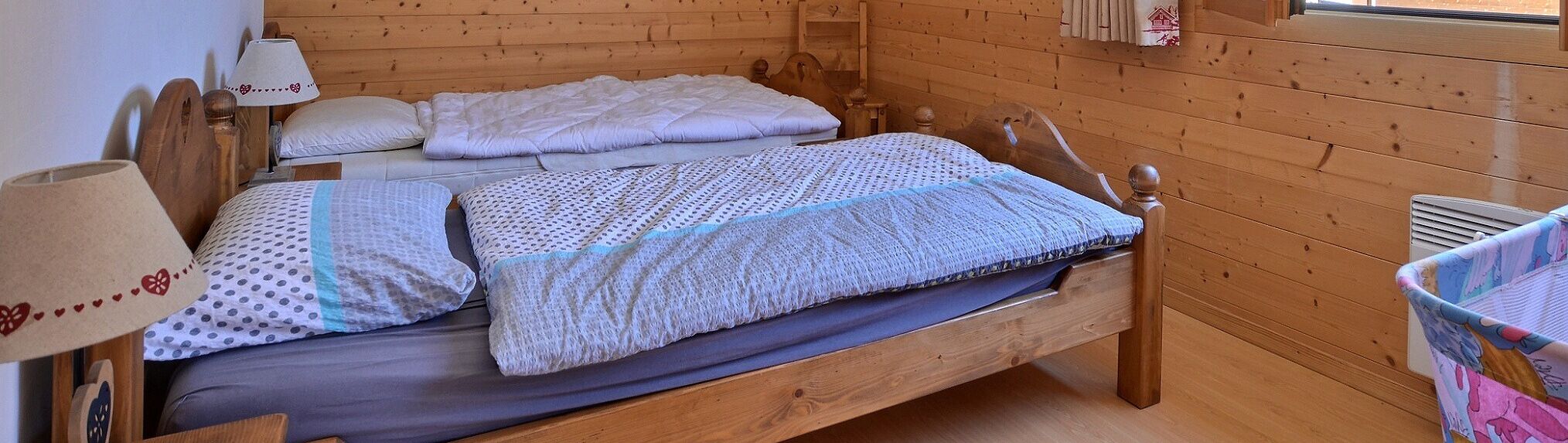 A wooden cabin room with a bed, pillows, and a nightstand with a lamp.