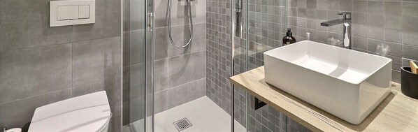 Un baño moderno con cabina de ducha de vidrio, lavabo blanco y retrete.
