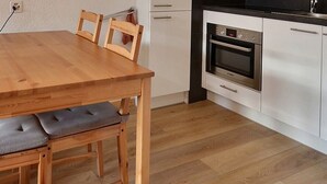 A wooden dining table with cushioned chairs, a modern kitchen with white cabinets and stainless steel appliances, and a floor lamp. - Comfortable flat for 4 people, living room, kitchen area, 1 2-bedroom, sleeping corner with 1 bunk b (Grimentz)
