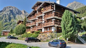 A multi-story building with balconies, set against a mountainous backdrop. - Comfortable flat for 4 people, living room, kitchen area, 1 2-bedroom, sleeping corner with 1 bunk b (Grimentz)