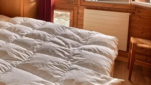 A bed with a white duvet, wooden headboard, and a window with curtains. - Comfortable flat for 4 people, living room, kitchen area, 1 2-bedroom, sleeping corner with 1 bunk b (Grimentz)