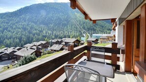 A balcony with a view of a forested mountain and traditional wooden buildings. - Comfortable flat for 6 people, living room with fireplace, kitchen area with dishwasher, 1 2-bedroom (Grimentz)