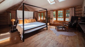 Ein Schlafzimmer in einer Blockhütte mit einem Himmelbett, Holzdielen und großen Fenstern.