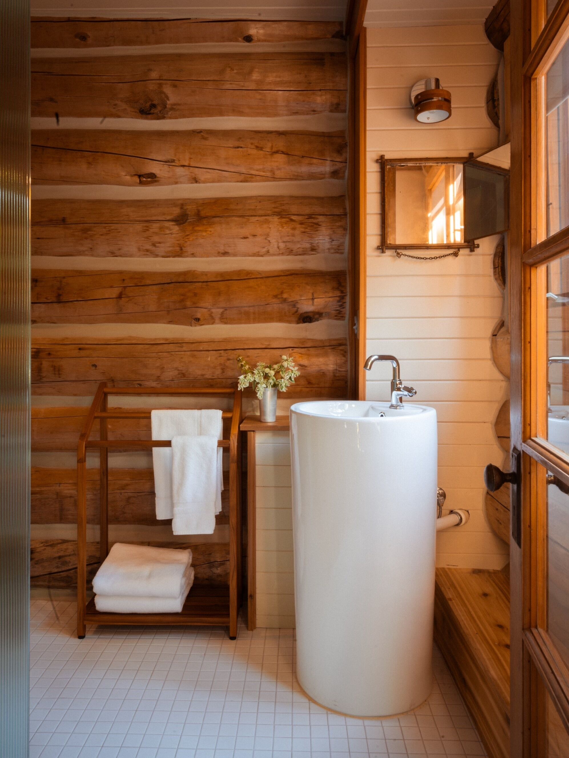 Ein Badezimmer mit Holzwänden, einem weißen Waschbecken, einem Handtuchhalter und einem kleinen Tisch mit einer Vase.