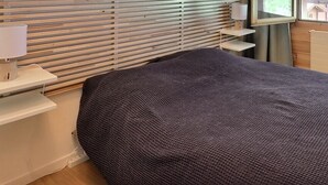 A bedroom with a bed, a bedside table with a lamp, a window with blinds, and a radiator. - Comfortable flat on 2 levels for 6 people, living room, kitchen area with dishwasher, 1 double bedro (Grimentz)