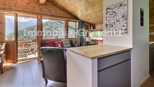 A cozy cabin interior with a wooden ceiling, a dining area with a table and chairs, a sofa with red cushions, and a view of mountains through large windows. - Comfortable flat on 2 levels for 6 people, living room, kitchen area with dishwasher, 1 double bedro (Grimentz)