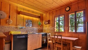 A wooden cabin kitchen with a central island, a dining table, and a window with a view of trees. - Comfortable traditional chalet on 2 levels for 7 to 8 people, living room, separated kitchen with di (Grimentz)